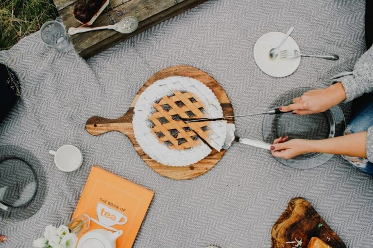 Food Fotograf Eine Person schneidet einen Kuchen mit einem Messer und serviert ihn mit einem Spatel auf einem Holzbrett.