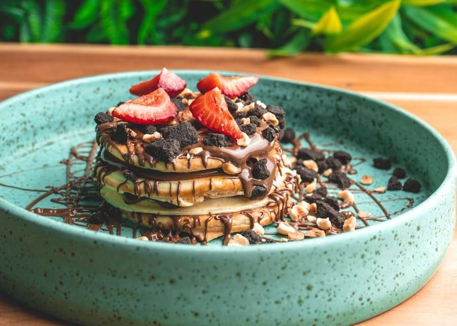 Der Food Fotograf - Ein Stapel Pfannkuchen mit Schokoladenüberzug, zerbröselten Keksen, gehackten Nüssen und geschnittenen Erdbeeren wird auf.