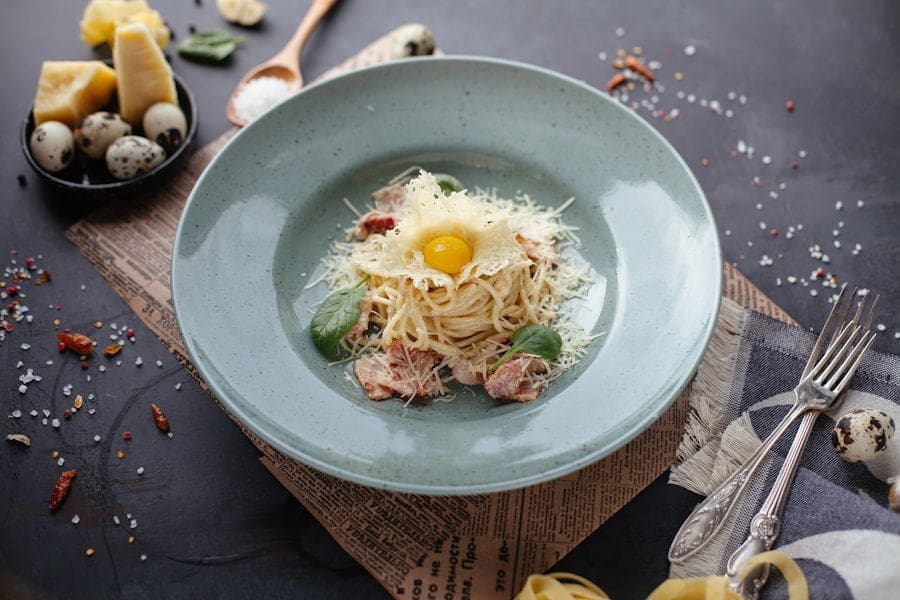 Food Fotograf Ein mit geriebenem Käse und einem Wachteleigelb belegtes Nudelgericht, serviert auf einem hellgrünen Teller.