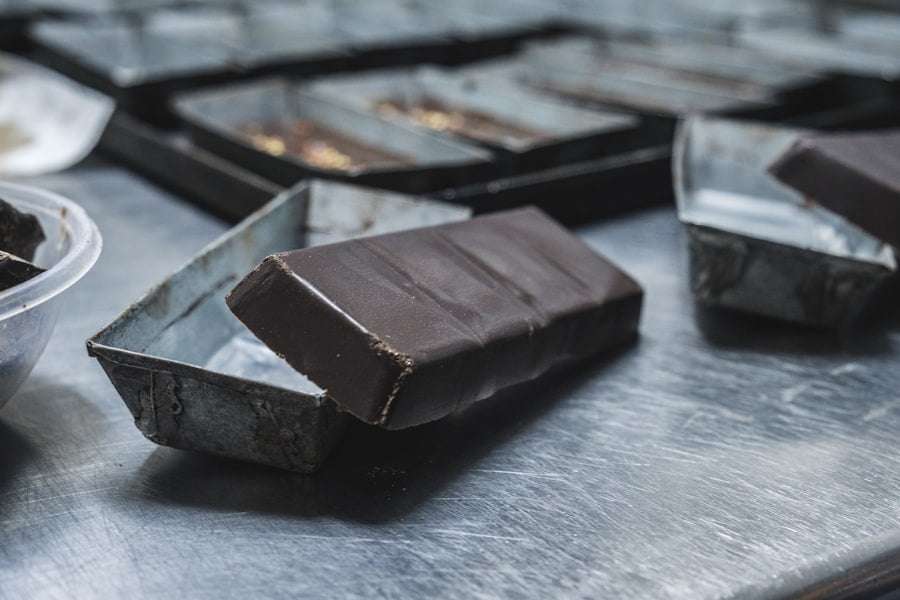 Der Food Fotograf - Eine Schokoladentafel, die teilweise aus einer rostigen Metallform gelöst wurde, liegt auf einer metallischen Oberfläche.