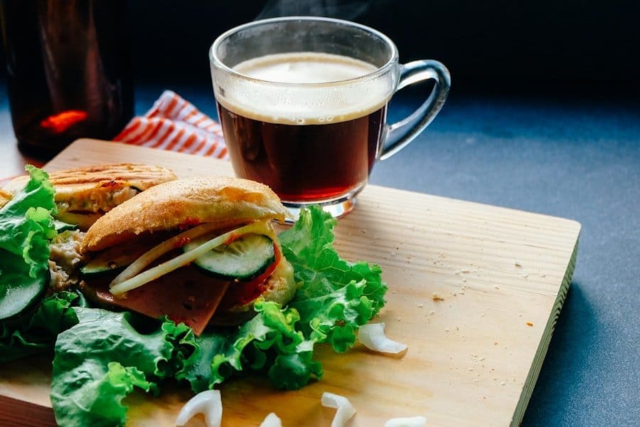 Food Fotograf Ein Sandwich mit Salat, Gurkenscheiben und Wurst liegt auf einem hölzernen Schneidebrett.