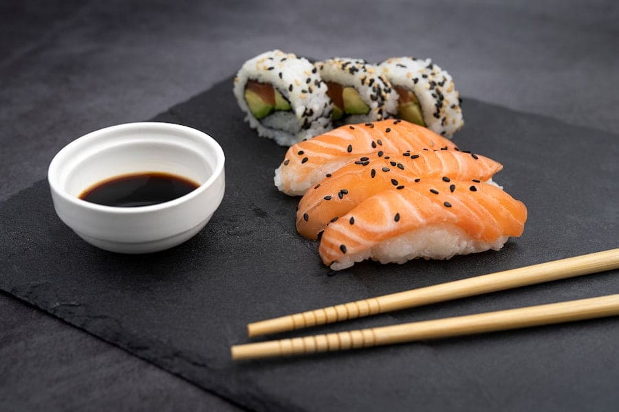 Der Food Fotograf - Auf einem Servierbrett aus Schiefer liegen drei Stücke Lachs-Nigiri mit schwarzem Sesam, zwei Stücke Sushi-Rolle mit Avocado.