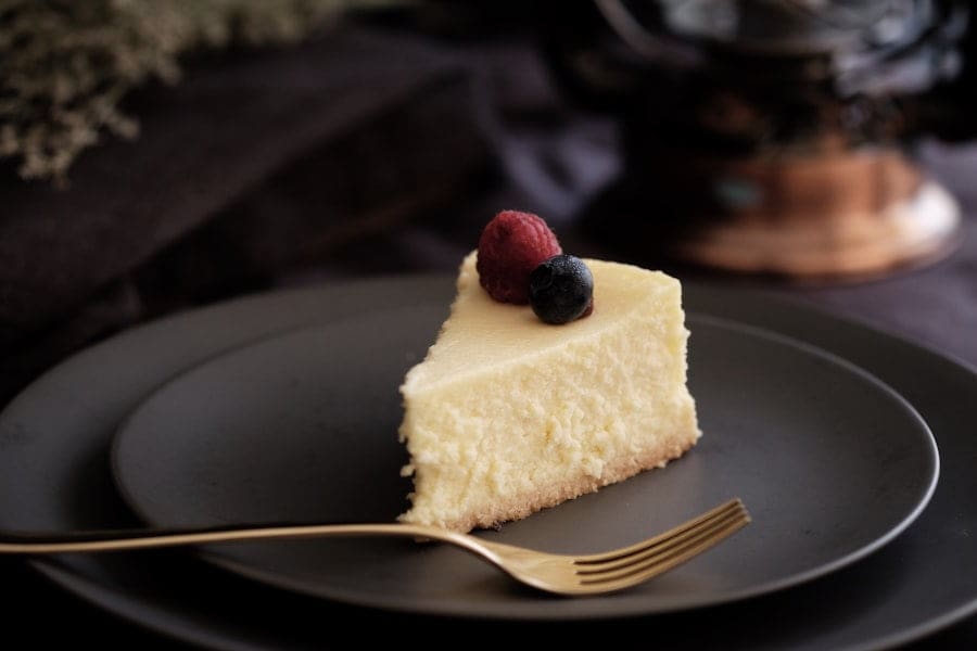 Der Food Fotograf - Ein Stück Käsekuchen mit Himbeeren und Blaubeeren liegt auf einem dunklen Teller.