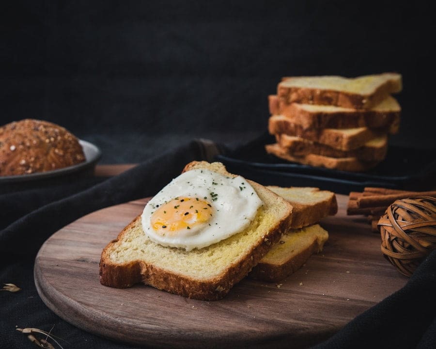 Der Food Fotograf - Ein gekochtes Spiegelei liegt auf einer Brotscheibe auf einem hölzernen Schneidebrett.