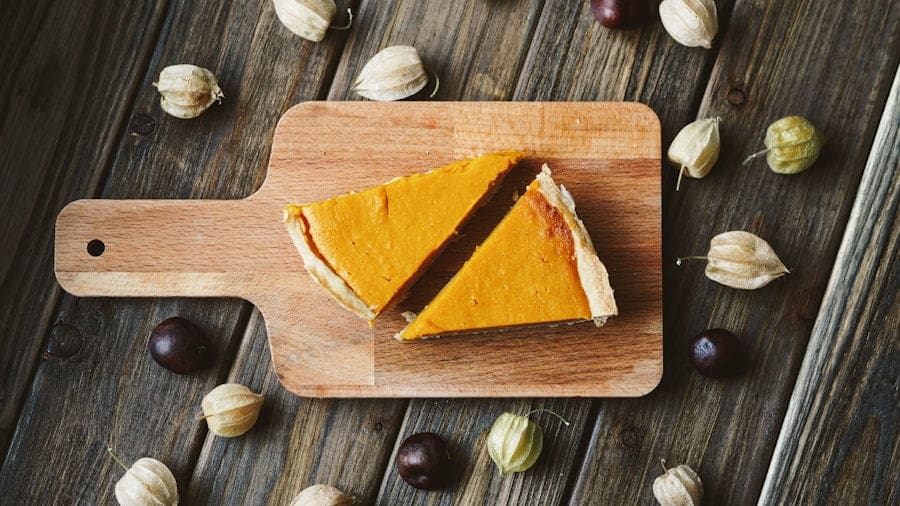 Food Fotograf Zwei Stücke Kürbiskuchen auf einem Holzschneidebrett, umgeben von Kapstachelbeeren und verstreuten dunklen Beeren auf einer.