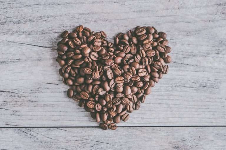 Der Food Fotograf - Eine Sammlung von Kaffeebohnen, die in Herzform auf einer grauen Holzoberfläche angeordnet sind.