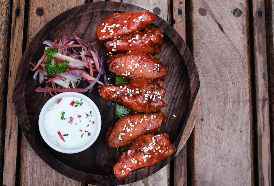 Der Food Fotograf - Ein Holzteller mit sechs Stück glasierten Hähnchenflügeln, bestreut mit Sesamkörnern, einer kleinen Portion Gemüsesalat und.