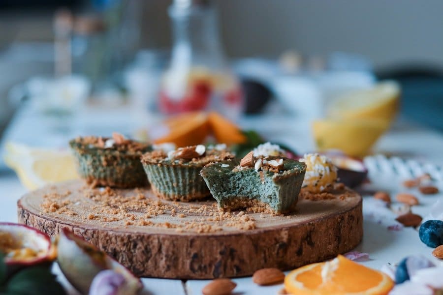Food Fotograf Eine Nahaufnahme eines Holzbretts, auf dem drei grünlich-braune Cupcakes mit gehackten Mandeln liegen.