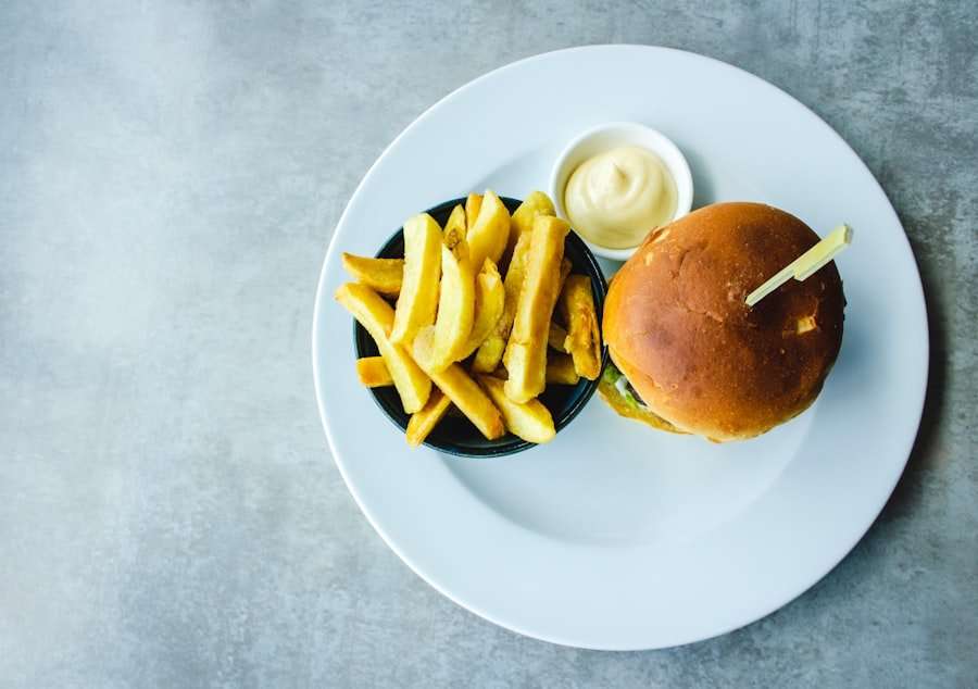 Draufsicht auf einen Teller mit einem Burger, einer kleinen Beilage aus Pommes Frites und einem kleinen Becher Dip-Sauce.