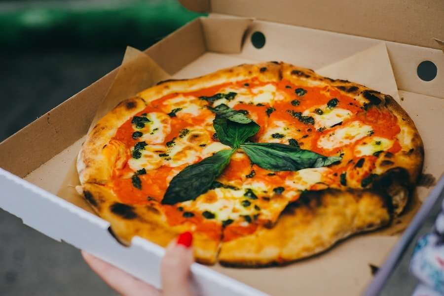 Eine im Holzofen gebackene Pizza mit einer knusprigen Kruste liegt in einem offenen Pizzakarton.