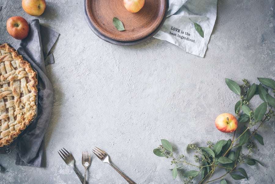 Der Food Fotograf - Eine Tischplatte mit Äpfeln, einem Kuchen, zwei Gabeln, einem dunklen Teller, einer Serviette mit dem Text „LIEBE ist die.