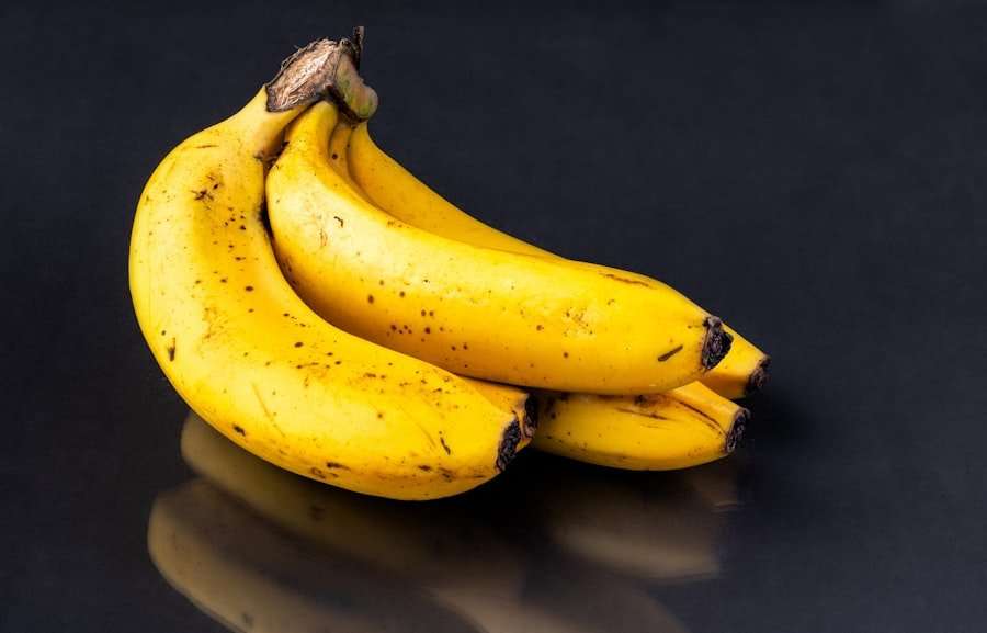 Der Food Fotograf - Ein kleines Bündel von fünf gelben Bananen mit kleinen braunen Flecken liegt auf einer dunklen, reflektierenden Oberfläche.