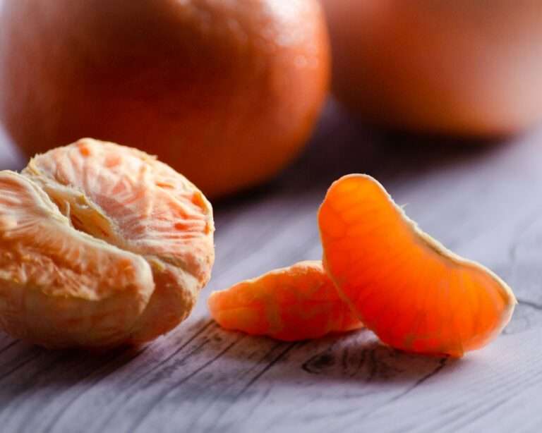 Nahaufnahme einer geschälten Mandarine mit drei abgetrennten Segmenten, die auf einer hellen Holzoberfläche liegen.