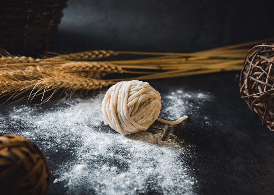 Der Food Fotograf - Ein Ball aus ungekochten Nudeln liegt auf einer dunklen, mit Mehl bestreuten Oberfläche.