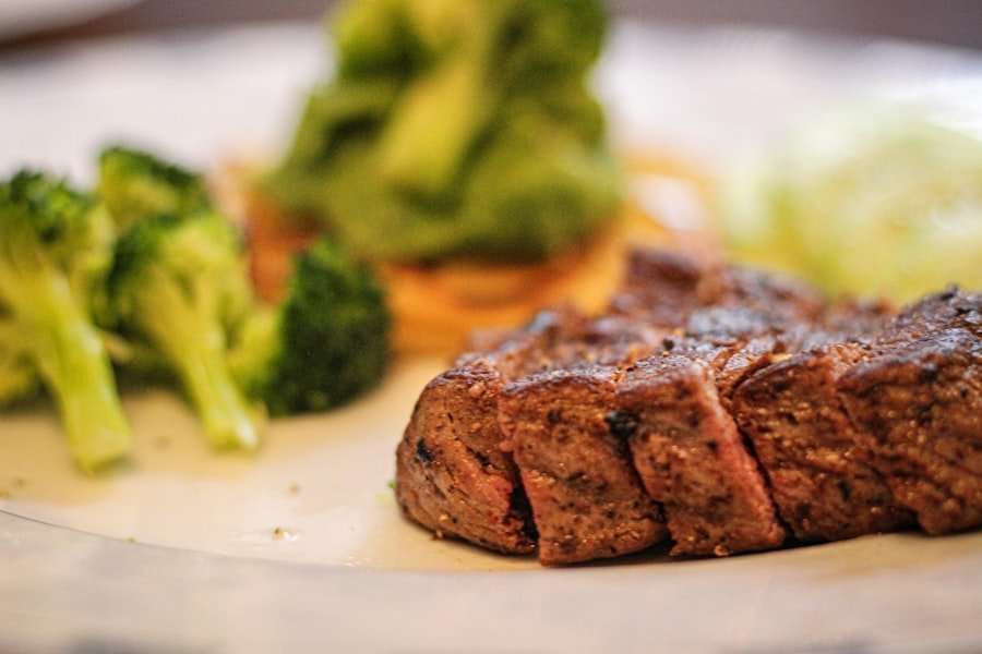 Ein Teller mit einem Stück gegrilltem Steak, Brokkoliröschen und einem grünen Blattgemüse im Hintergrund.