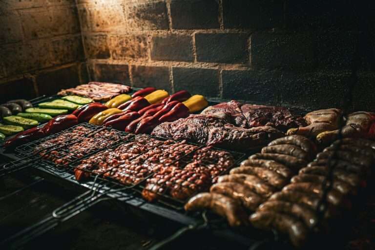 Verschiedene Fleischsorten, Wurst und Gemüse, darunter Paprika und Zucchini, werden über offener Flamme gegrillt.