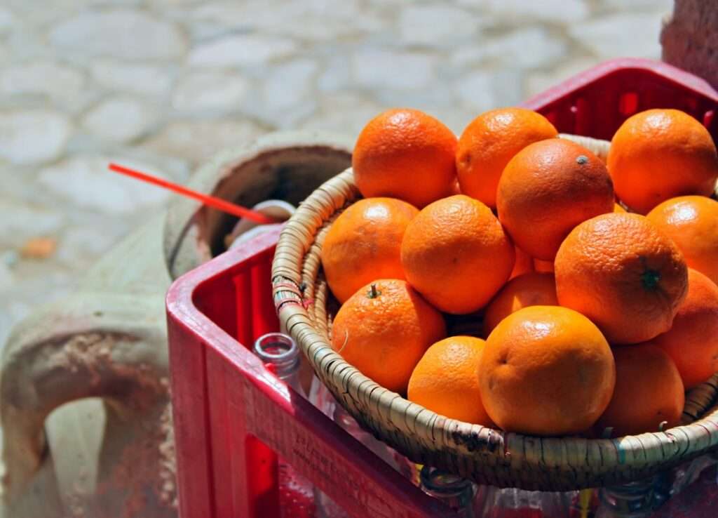 Ein mit Orangen gefüllter geflochtener Korb steht auf einer umgedrehten roten Plastikkiste.