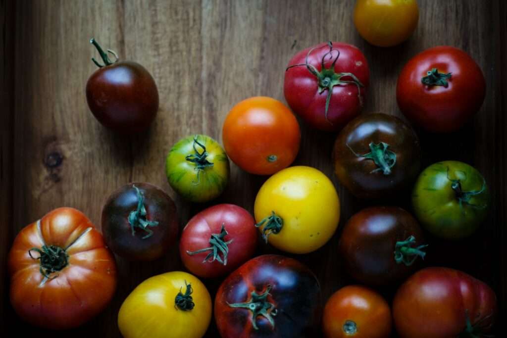 Eine Holzoberfläche ist mit verschiedenen Sorten von Heirloom-Tomaten in verschiedenen Farben wie Rot, Gelb, Grün und Braun bedeckt.