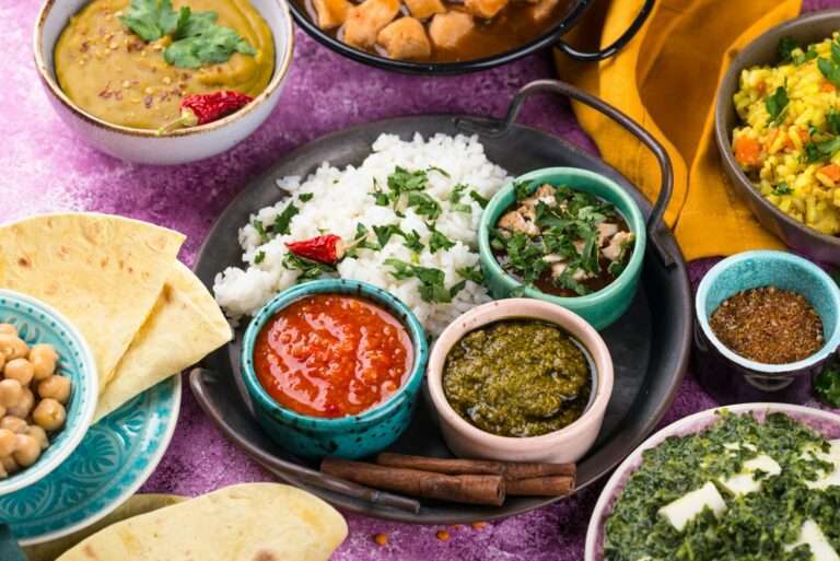 Eine Auswahl indischer Gerichte ist kunstvoll auf einem Tisch arrangiert, darunter Schüsseln mit Curry, Reis, Chutneys und Linsen mit Naan-Brot.