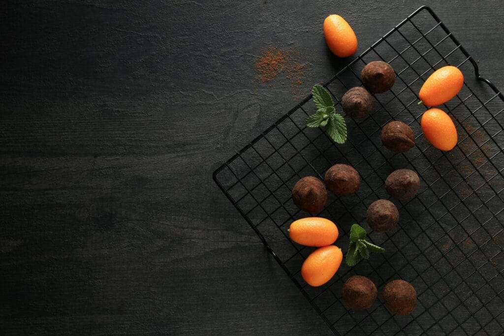 Auf einem Abkühlgitter sind Pralinen und Kumquats ordentlich angeordnet.
