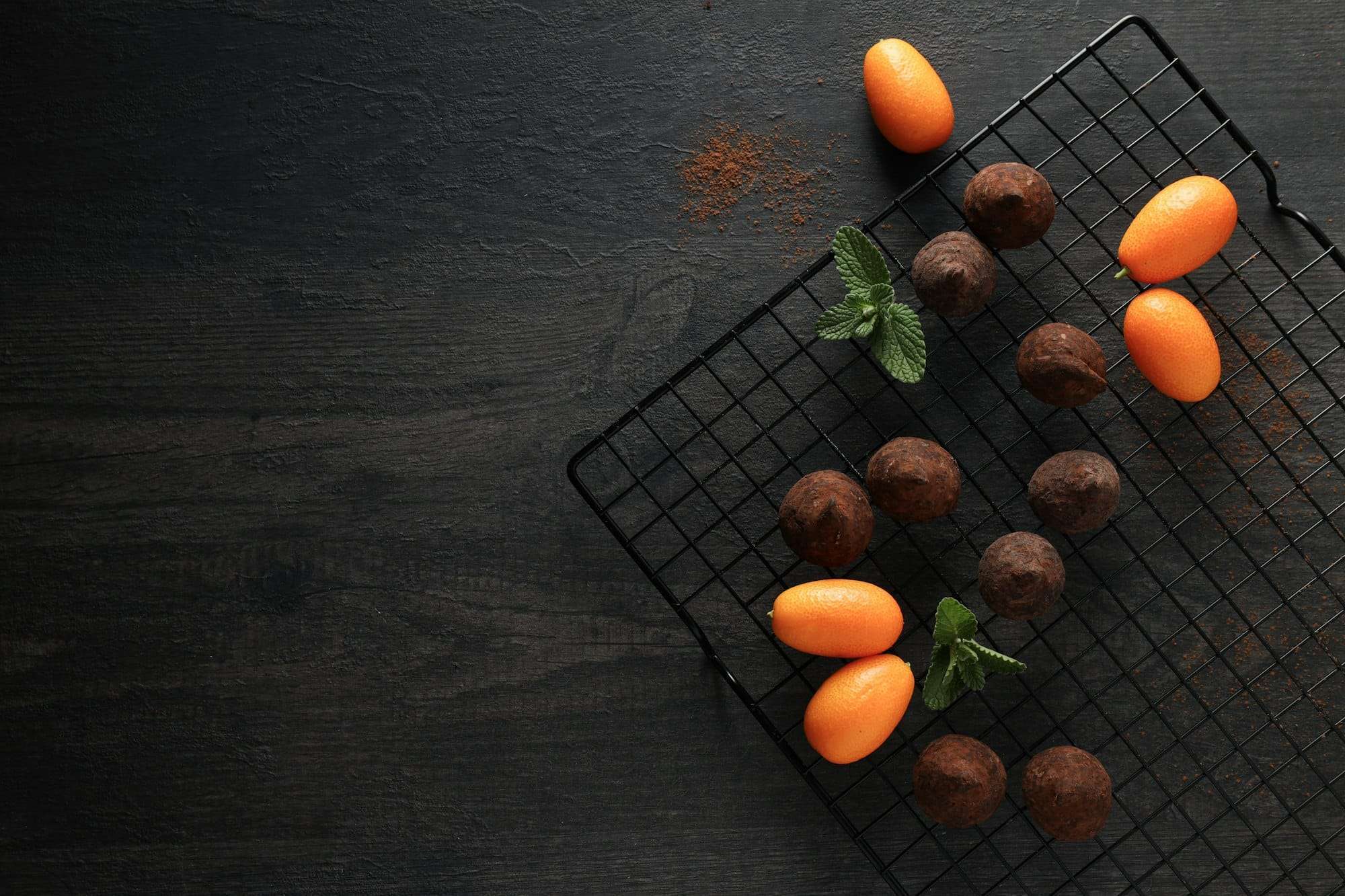 Auf einem Abkühlgitter sind Pralinen und Kumquats ordentlich angeordnet.