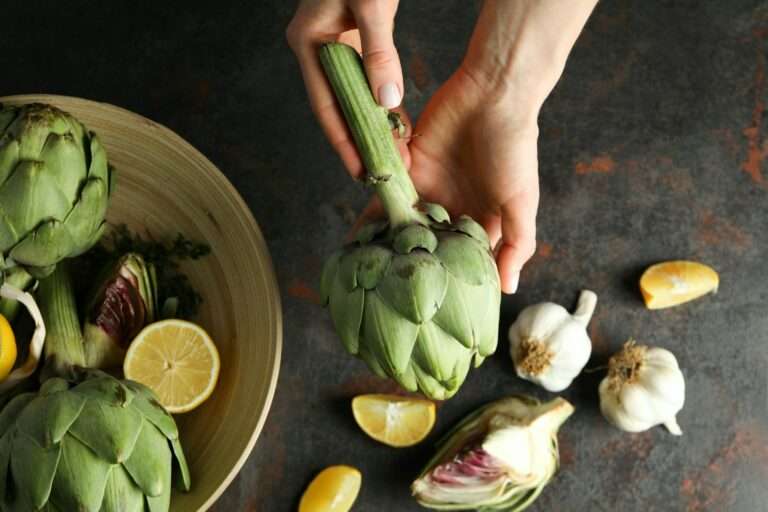 Eine Person hält eine Artischocke über einem dunklen Food-Fotografie-Hintergrund.