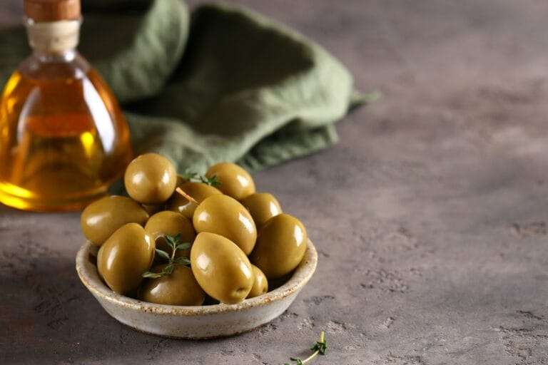Eine kleine Keramikschale voller grüner Oliven steht auf einer strukturierten Oberfläche und fängt die Essenz der Food-Fotografie ein.