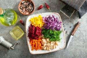 Ein Teller mit verschiedenen Gemüsesorten, darunter Mais, zerkleinerter Rotkohl, geriebene Rote Bete, geriebene Karotten, Dill und weiße Bohnen.