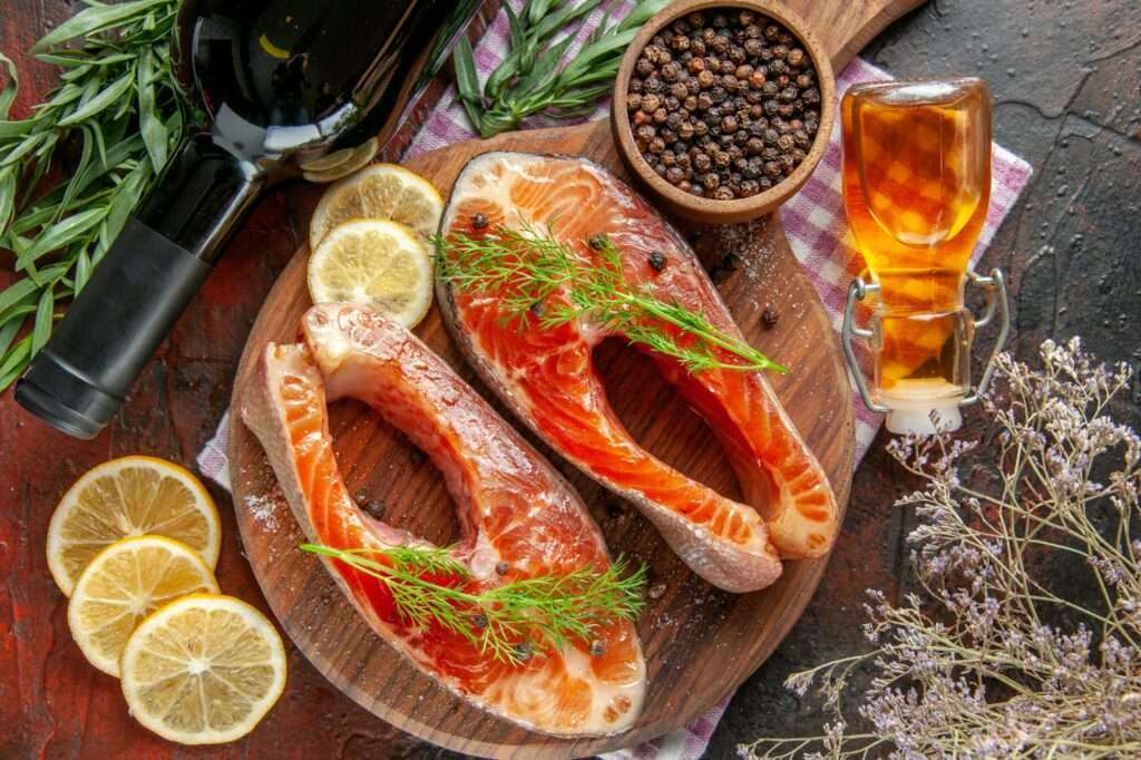 Zwei rohe Lachssteaks mit Dill liegen auf einem runden Holzschneidebrett, umgeben von Zitronenscheiben, einer Flasche Wein und einer kleinen.