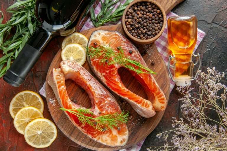 Zwei rohe Lachssteaks mit Dill liegen auf einem runden Holzschneidebrett, umgeben von Zitronenscheiben, einer Flasche Wein und einer kleinen.
